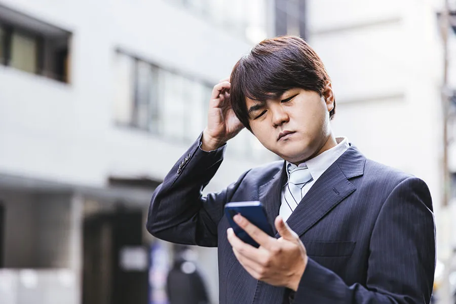 困った表情でスマートフォンを見つめる男性