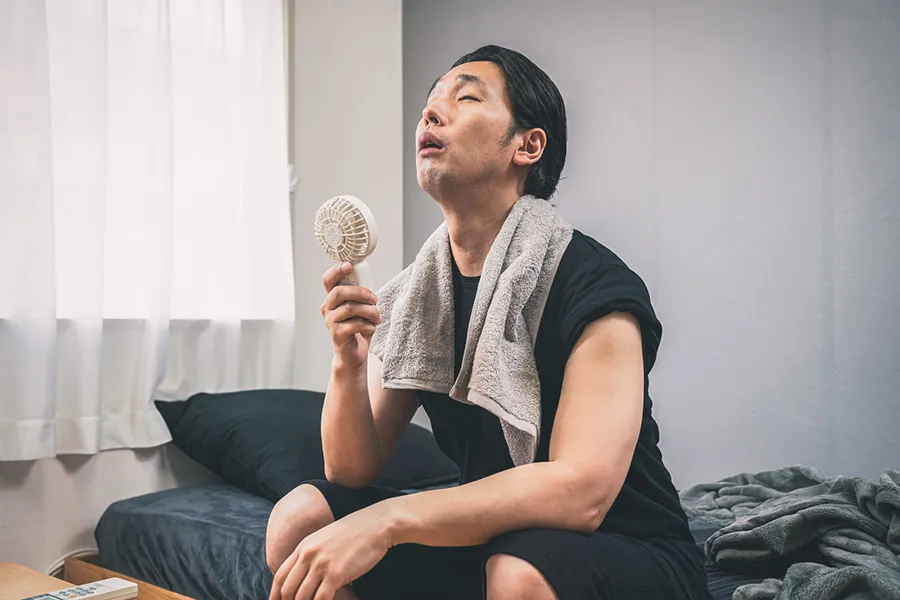 扇風機を回す暑そうな表情の男性